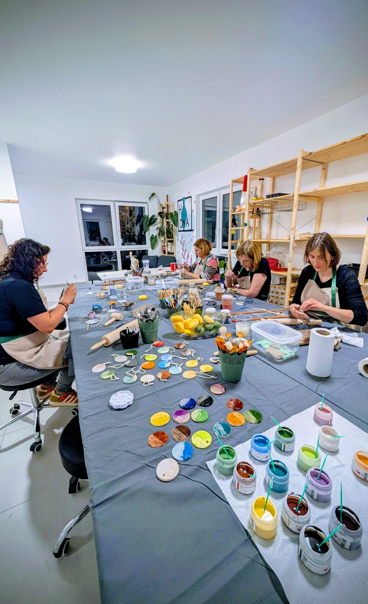 Uczestnicy warsztatów przy stole, farby i ceramiczne elementy